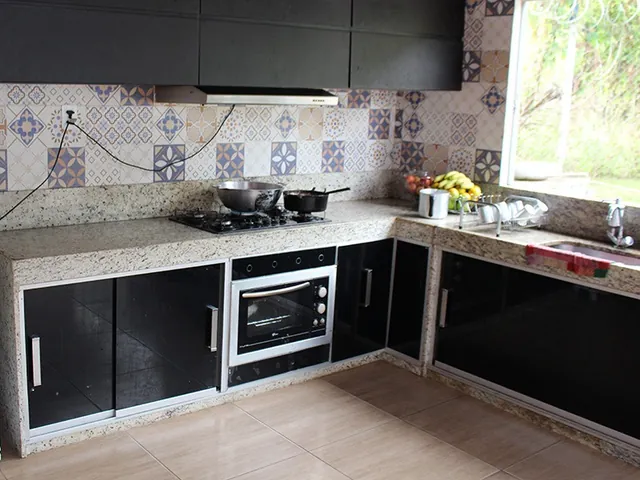 Cozinha com bancada de granito, fogão a gás de embutir, forno, armários pretos e azulejos estampados